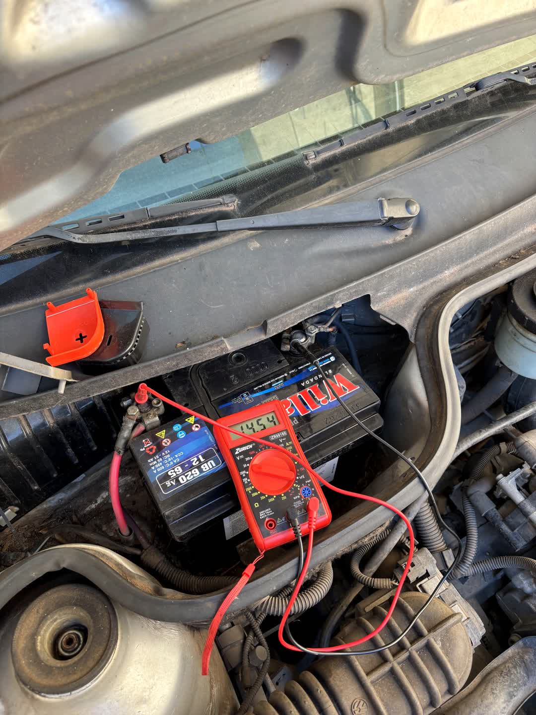 Téster conectado a la batería de un auto en el vano motor