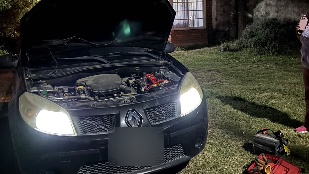Auto de noche frente a una casa, con el capó abierto y las luces encendidas, durante un auxilio